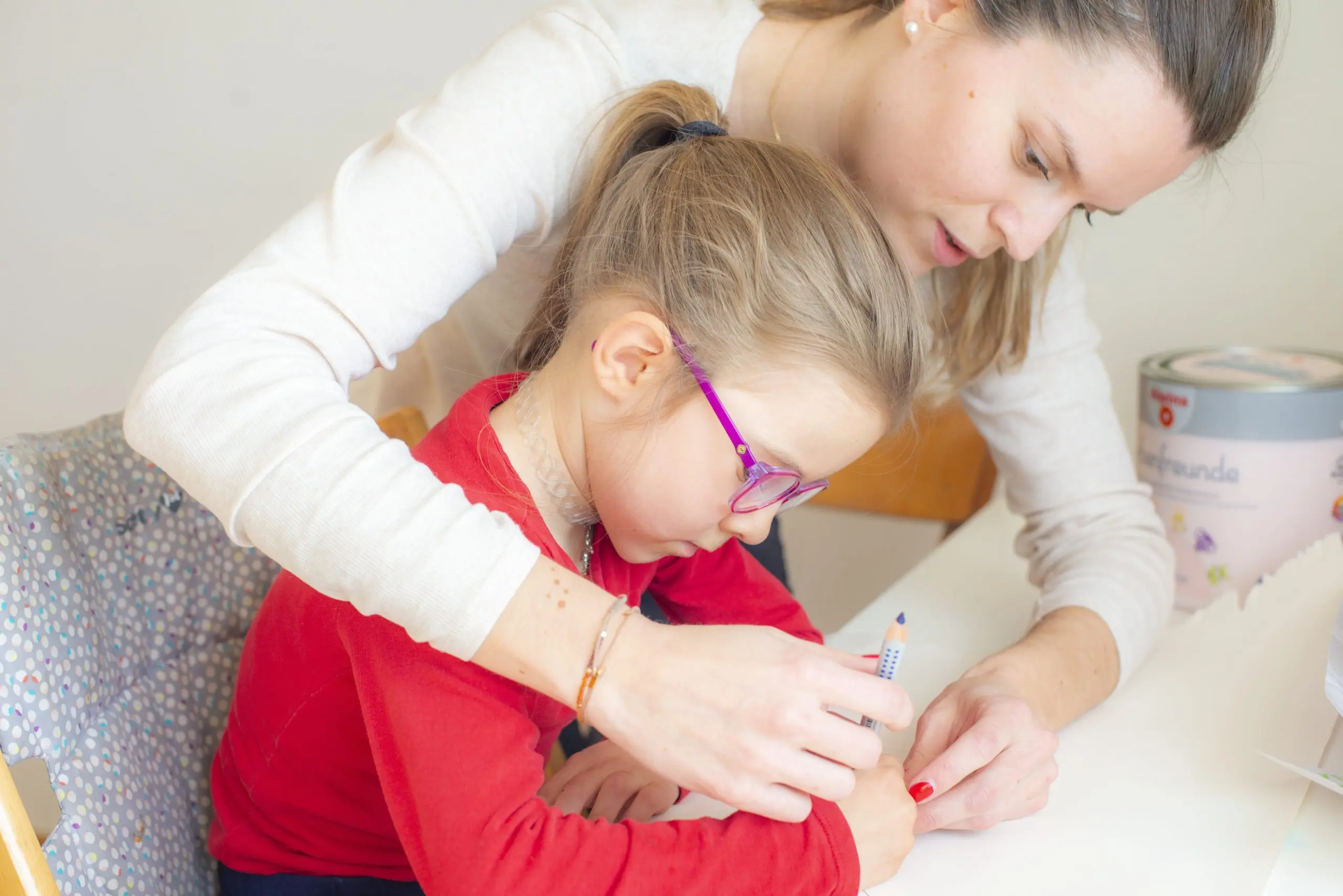 Ergotherapeutin führt die Hand eines Mädchens beim Schreiben