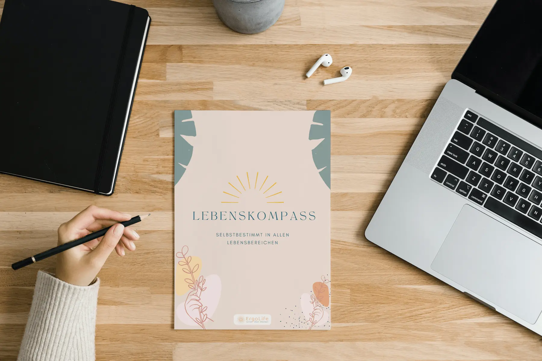 Heft „Lebenskompass“ auf einem Holztisch zwischen Laptop und Tablet