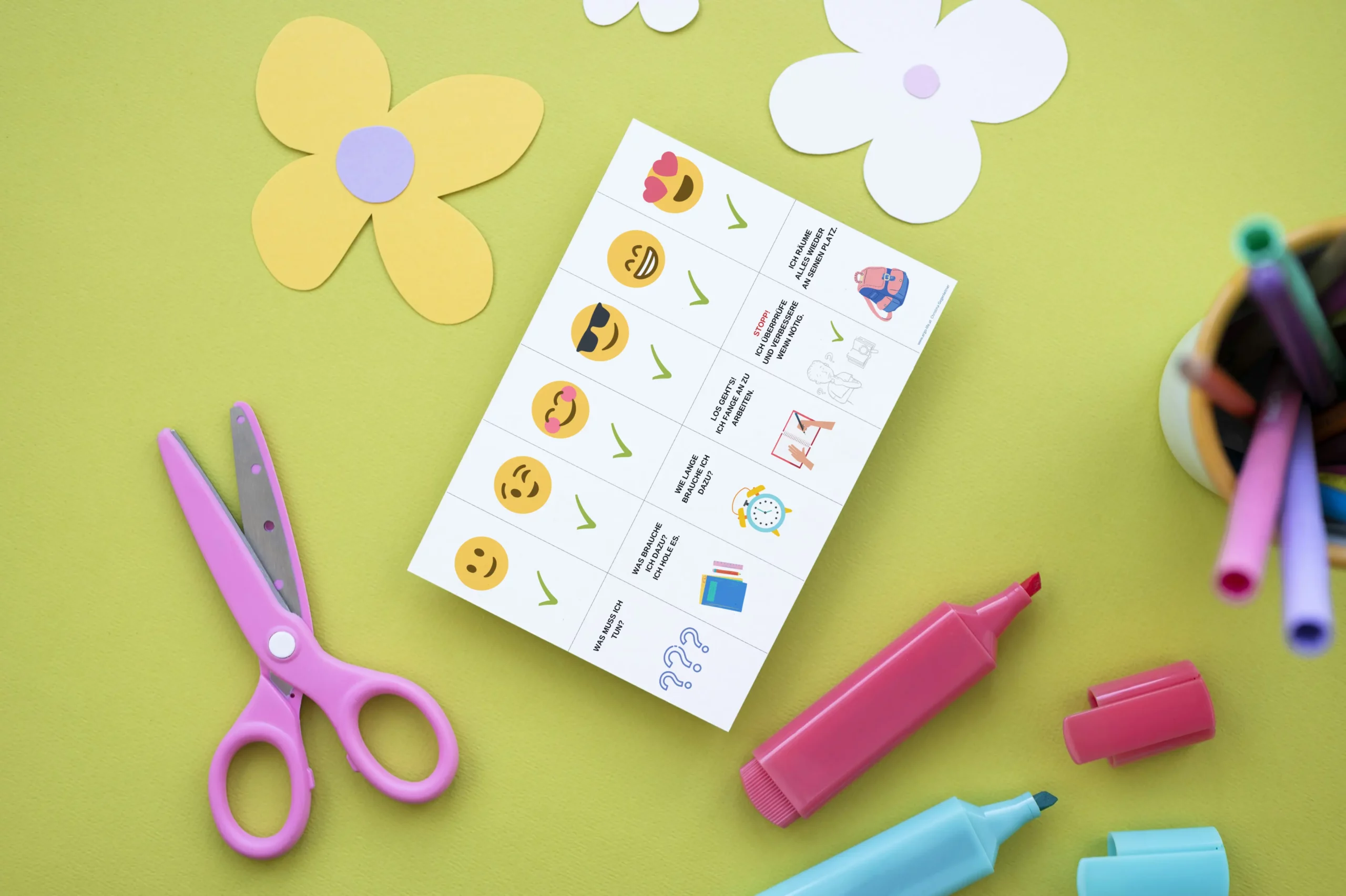 Ausgedruckter Aufgabenhelfer mit Smileys neben Schere und Stiften