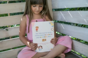 Mädchen hält lächelnd das Arbeitsbuch „Auf der Suche nach fröhlichen Gedanken und Superkräften“